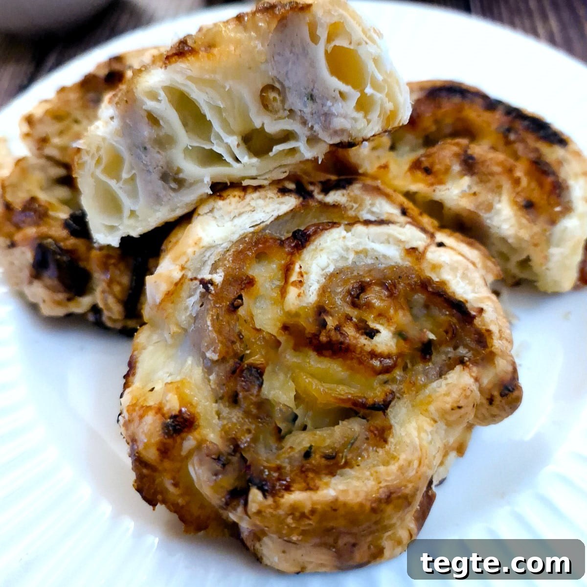 Savory Sausage and Caramelized Onion Pinwheel Appetizers 14 2 sausage and onion pinwheels on a white plate with a third one cut open to show the inside.