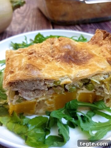A slice of butternut, leek and sausage pie on a white plate.