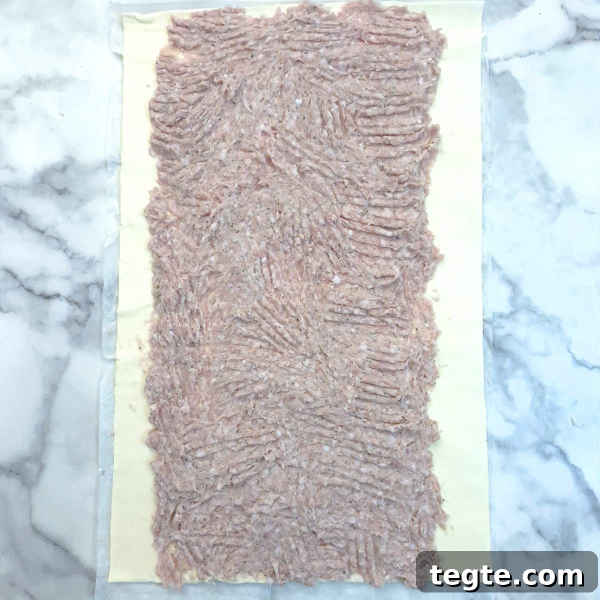 Savory Sausage and Caramelized Onion Pinwheel Appetizers 7 Sausage meat spread onto a sheet of puff pastry.
