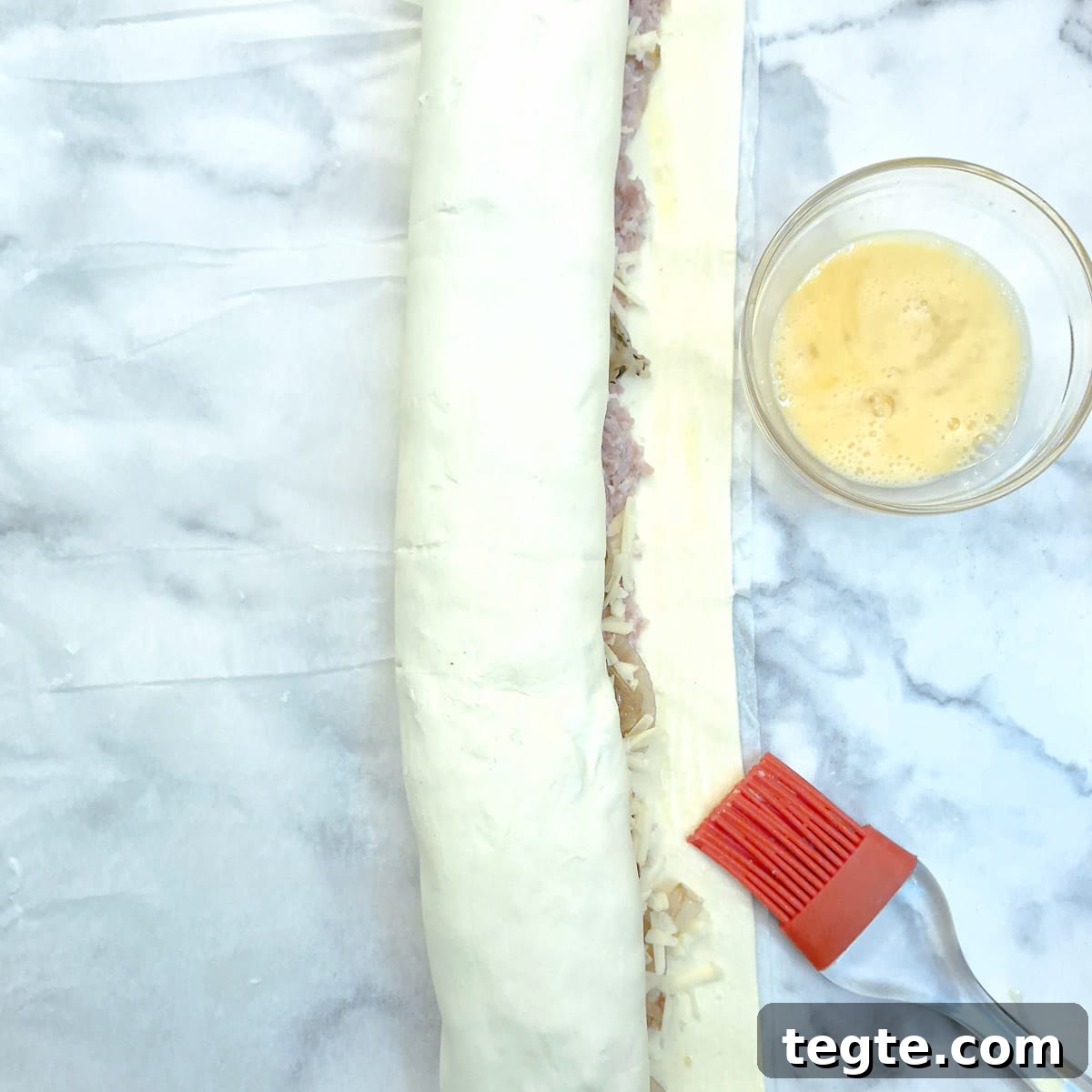 Savory Sausage and Caramelized Onion Pinwheel Appetizers 10 A rolled sausage roll being sealed with egg wash.