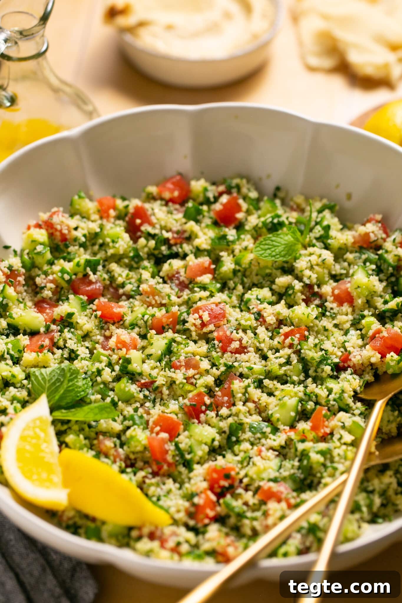 a bowl filled with fresh ingredients for salad with gold serving spoons. 