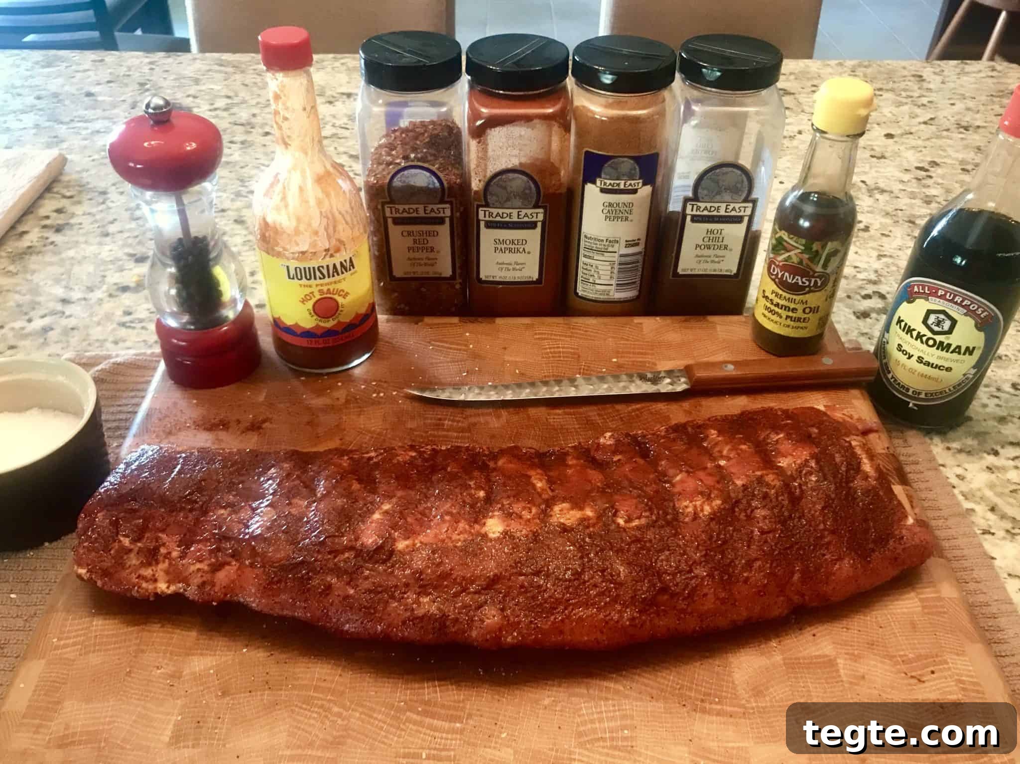 Rack of ribs on wooden cutting board with spices lined up behind it close up view