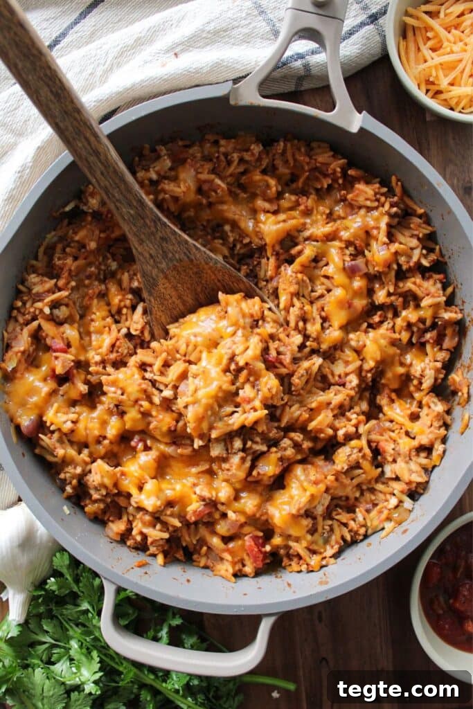 Cheesy Taco Rice Skillet — One-Pan Weeknight Dinner 5 A large skillet of cheesy taco rice with a spoon
