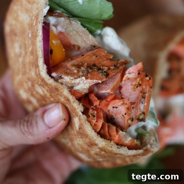 Healthy Broiled Salmon Gyros pita cut in half stuffed with broiled salmon and a white sauce with a side of spinach