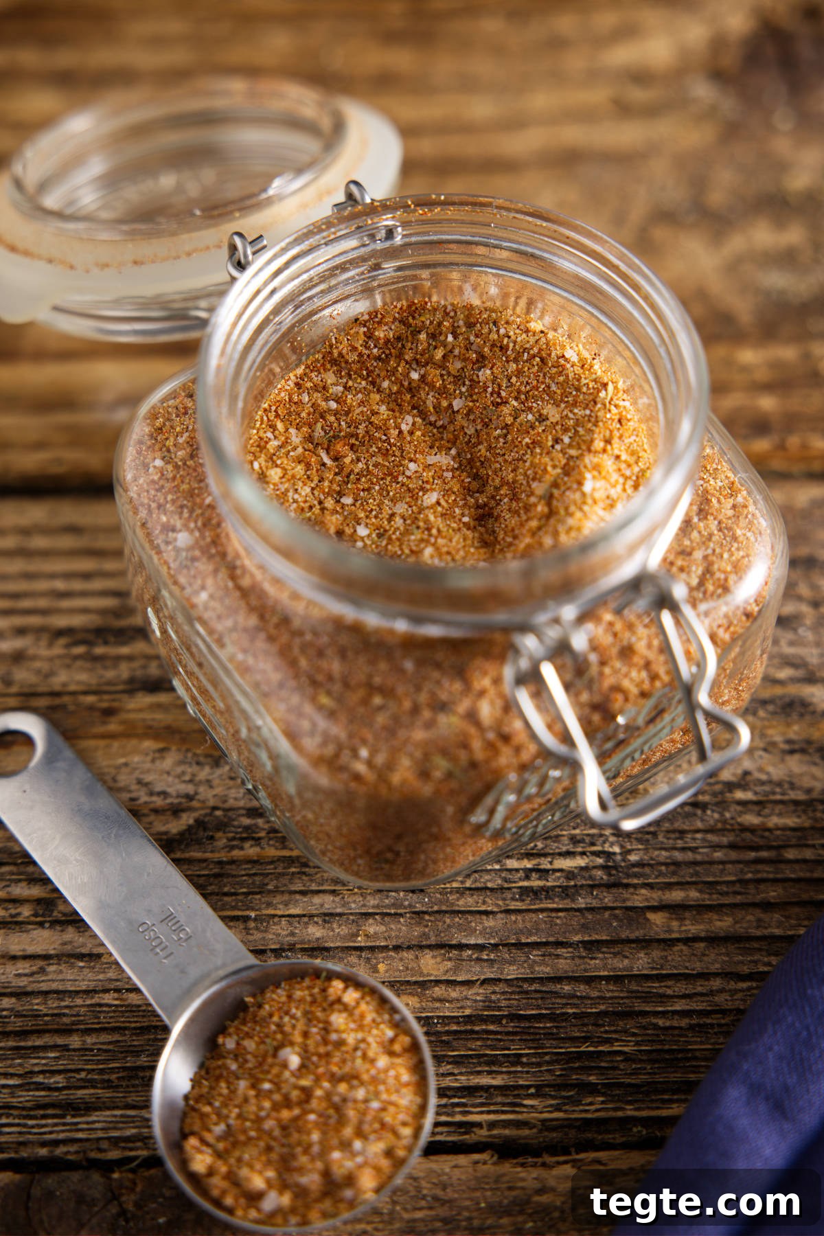 Smoked pork loin dry rub in glass container with a tablespoon of seasoning next to it.