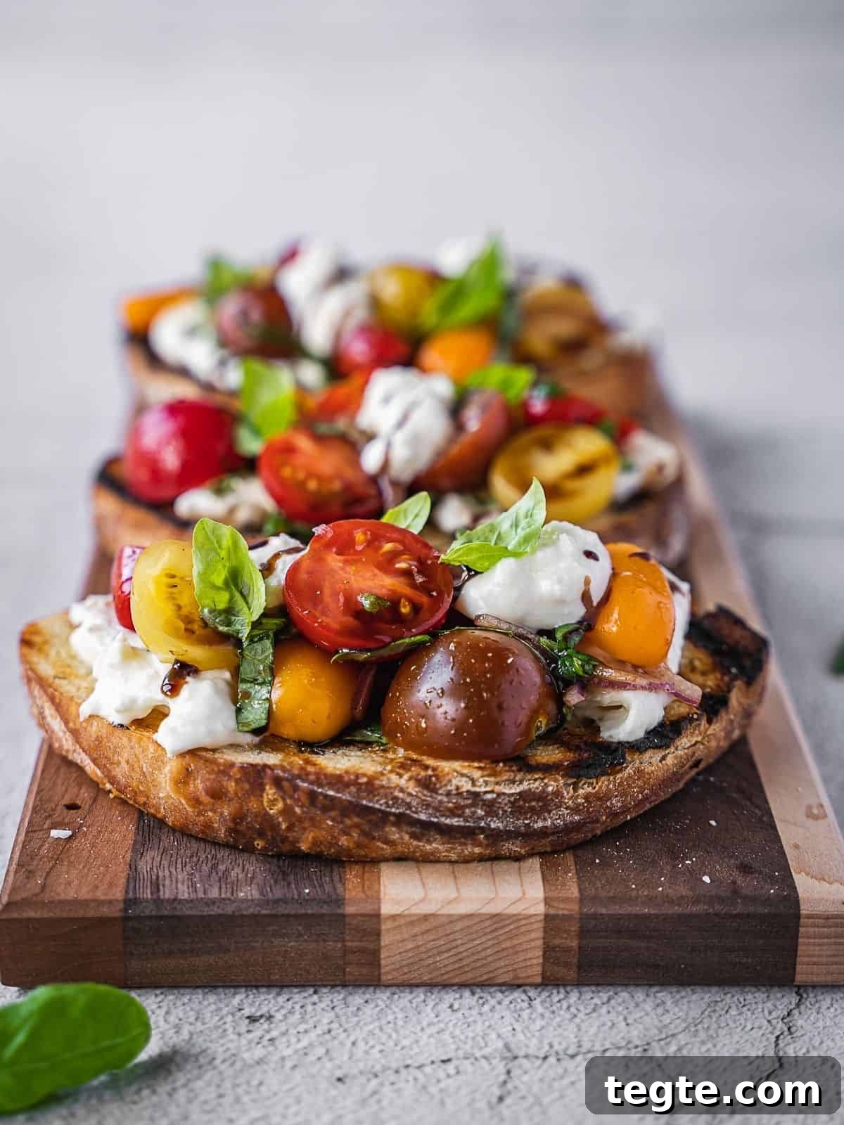 Creamy Burrata Bruschetta with Heirloom Tomatoes and Basil 3 cherry tomatoes and burrata cheese on toasted bread, served on a wooden board.