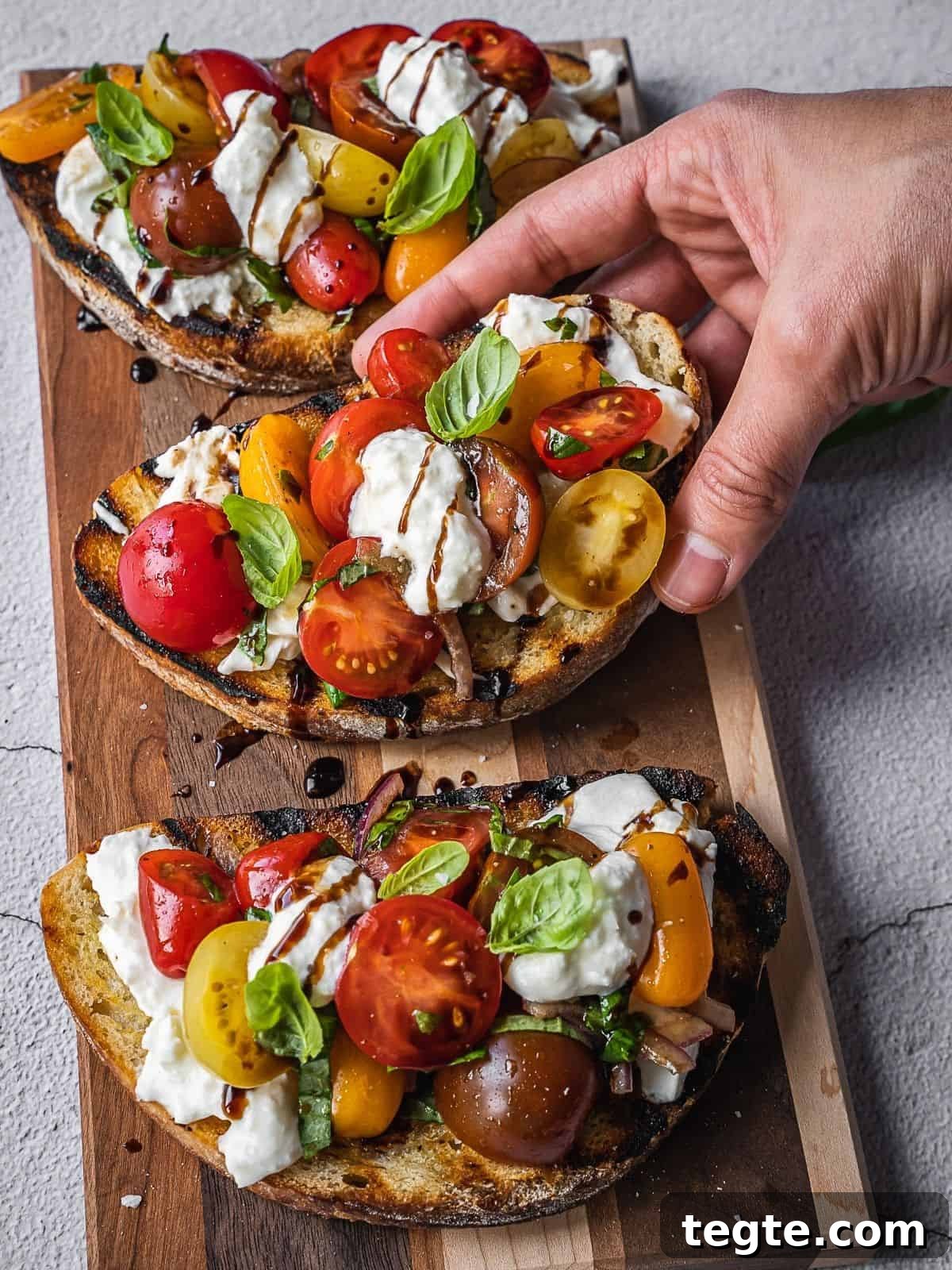 Creamy Burrata Bruschetta with Heirloom Tomatoes and Basil 9 A hand holding a burrata bruschetta with tomatoes and basil.