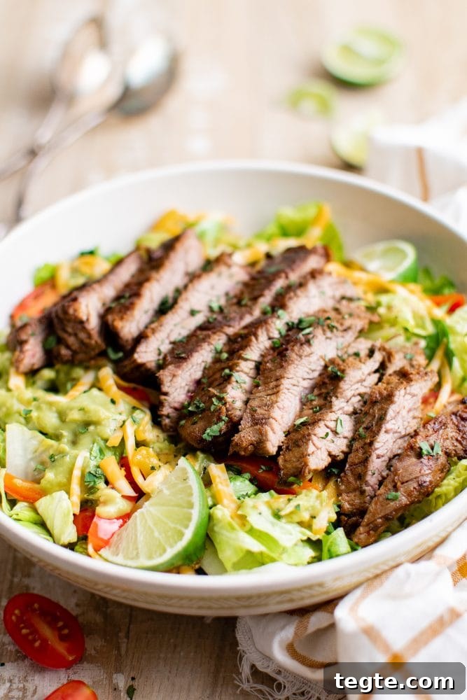 picture of steak fajita salad with guacamole on a white plate on a table