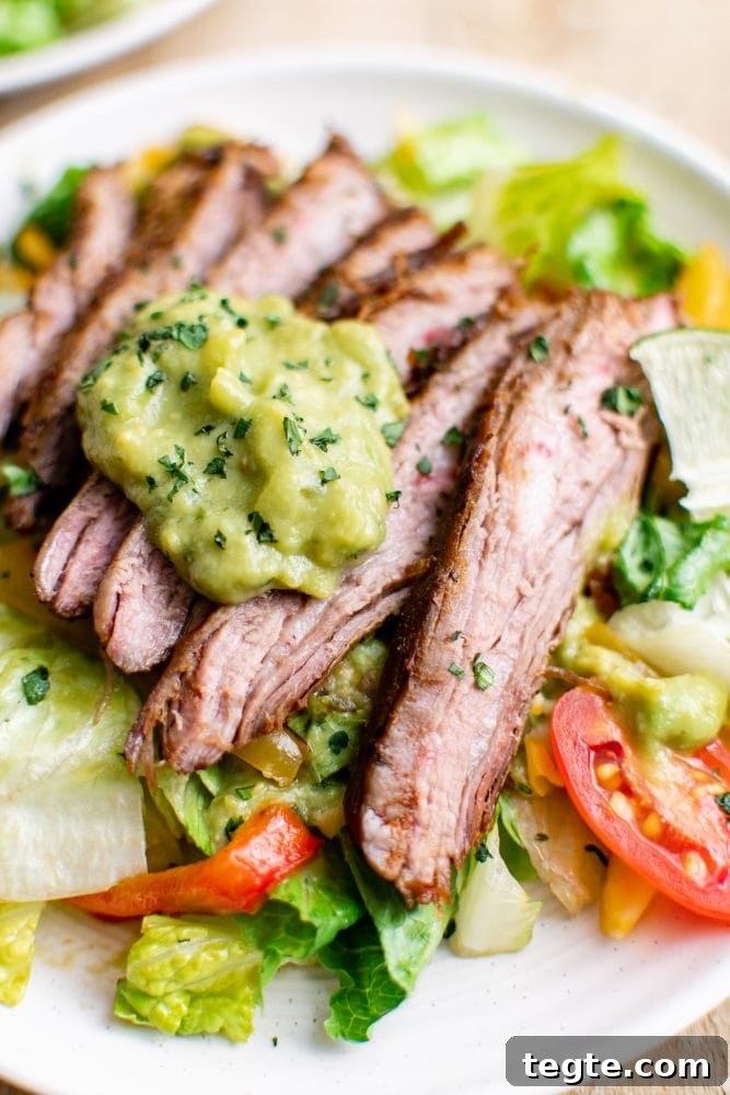 picture of steak fajita salad with guacamole on a white plate on a table