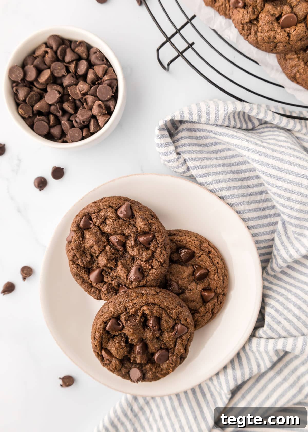 Ultimate Double Chocolate Cookies Recipe: Moist, Fudgy Bites 9 Double chocolate chip cookies on a plate next to a bowl of chocolate chips.