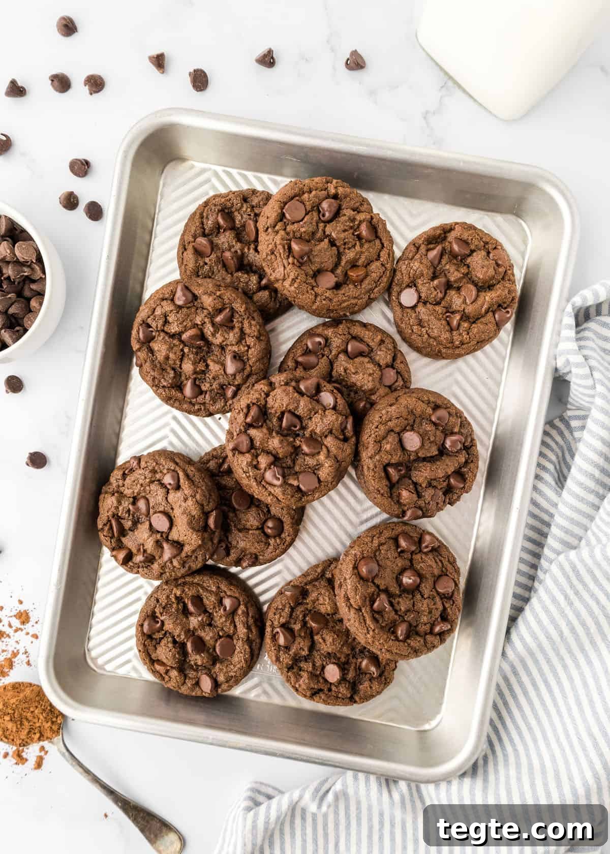 Ultimate Double Chocolate Cookies Recipe: Moist, Fudgy Bites 10 Double chocolate chip cookies on a baking sheet on a counter with chocolate chips.