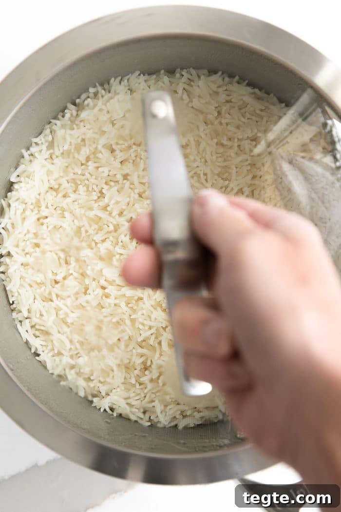 Perfect Basmati Rice on the Stove: Fluffy, No Rice Cooker Needed 3 Perfectly cooked basmati rice in a small pot covered with a glass lid held by it's handle by a hand.