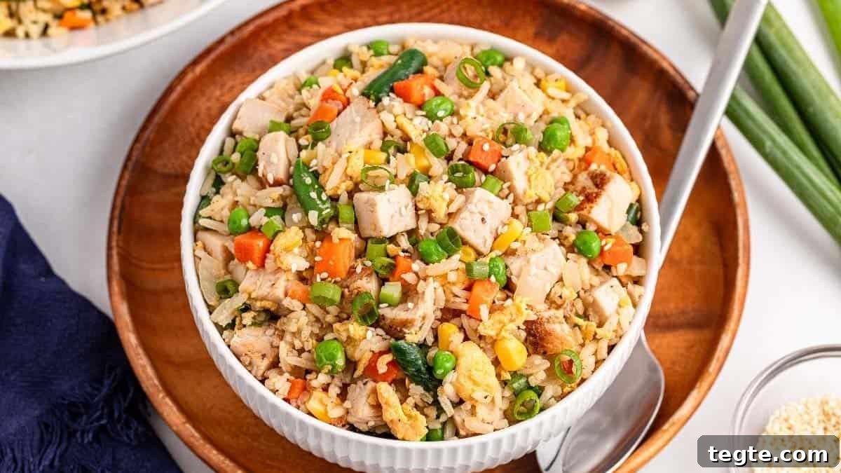 15 Creative Post-Thanksgiving Dinners to Transform Leftovers 2 A bowl of chicken fried rice with vegetables like peas, carrots, corn, and green beans—served with a spoon on a wooden plate—makes for one of the perfect budget-friendly post-Thanksgiving dinners.