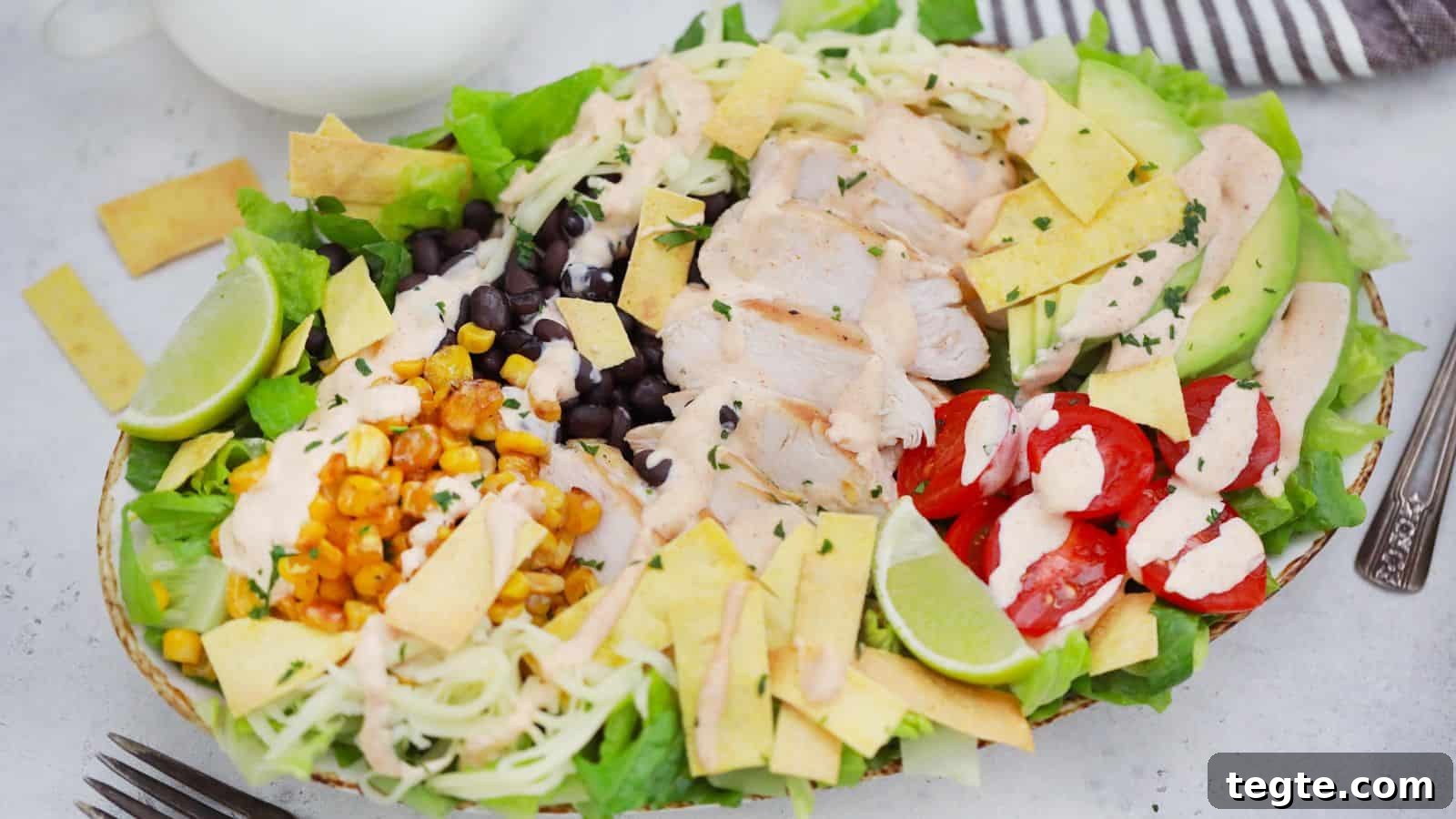 15 Creative Post-Thanksgiving Dinners to Transform Leftovers 5 A colorful chicken salad with avocado, black beans, corn, cherry tomatoes, and lime slices, presented in a white bowl.