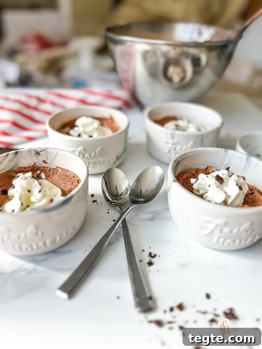 Decadent 3-Ingredient Chocolate Mousse Recipe 3 Individual cups filled with chocolate mousse and topped with whipped cream and shaved chocolate on a white background.