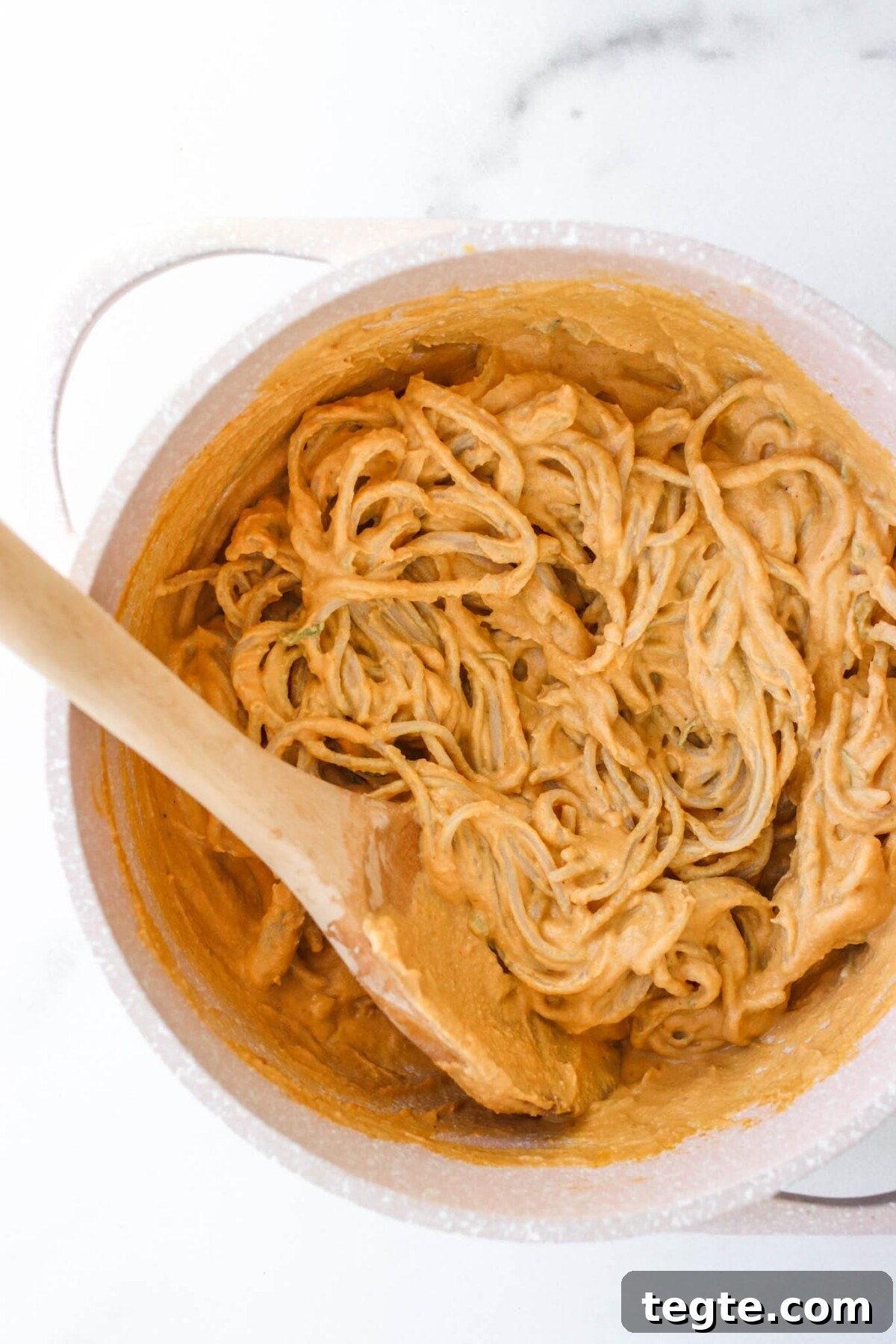 Creamy Pumpkin Tahini Pasta in 10 Minutes: Quick Weeknight Recipe 4 a bowl with chickpea spaghetti and pumpkin tahini sauce in a bowl with a wooden spoon.