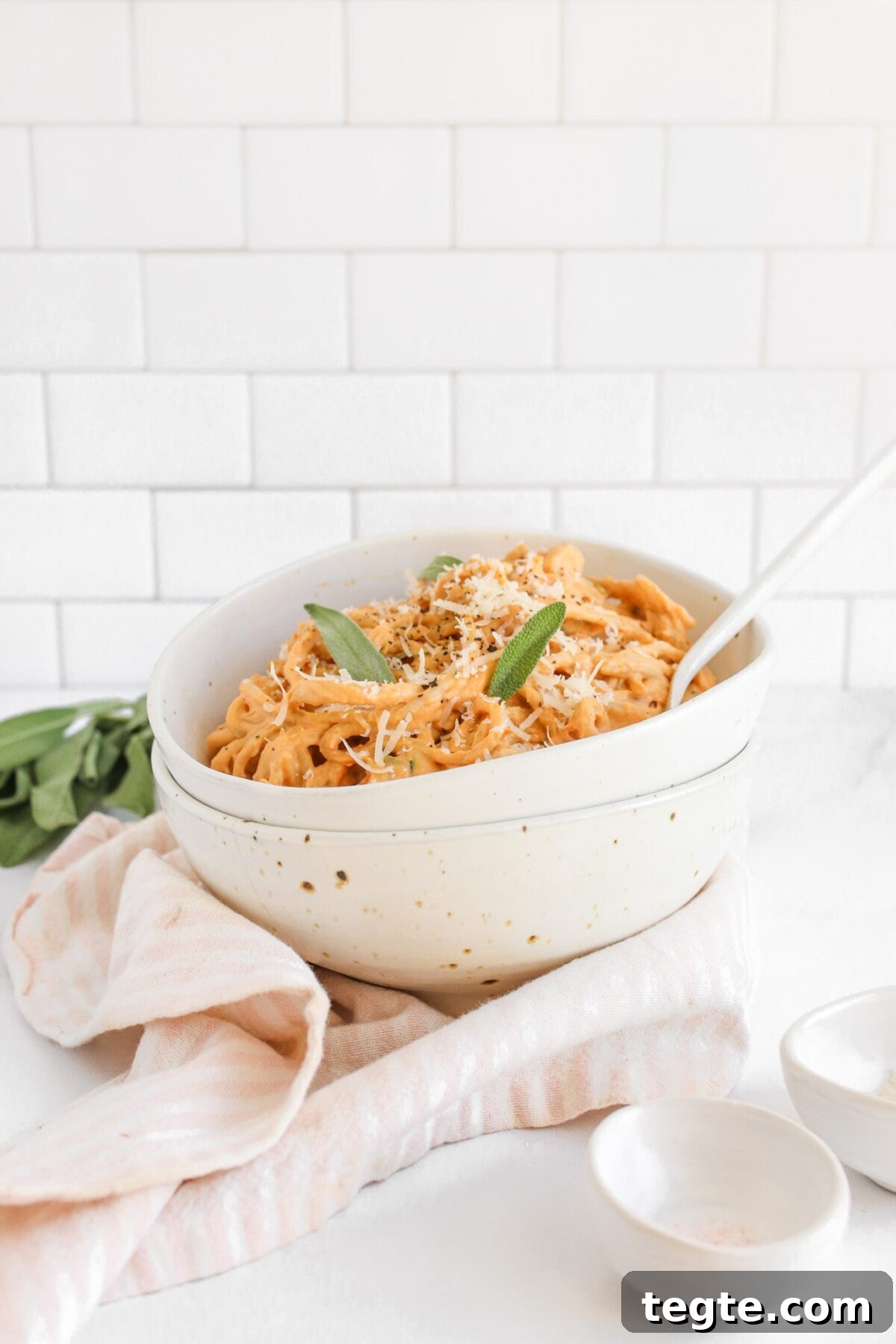 Creamy Pumpkin Tahini Pasta in 10 Minutes: Quick Weeknight Recipe 5 a side view of a bowl of pasta topped with fresh sage and a white spoon resting on the side.