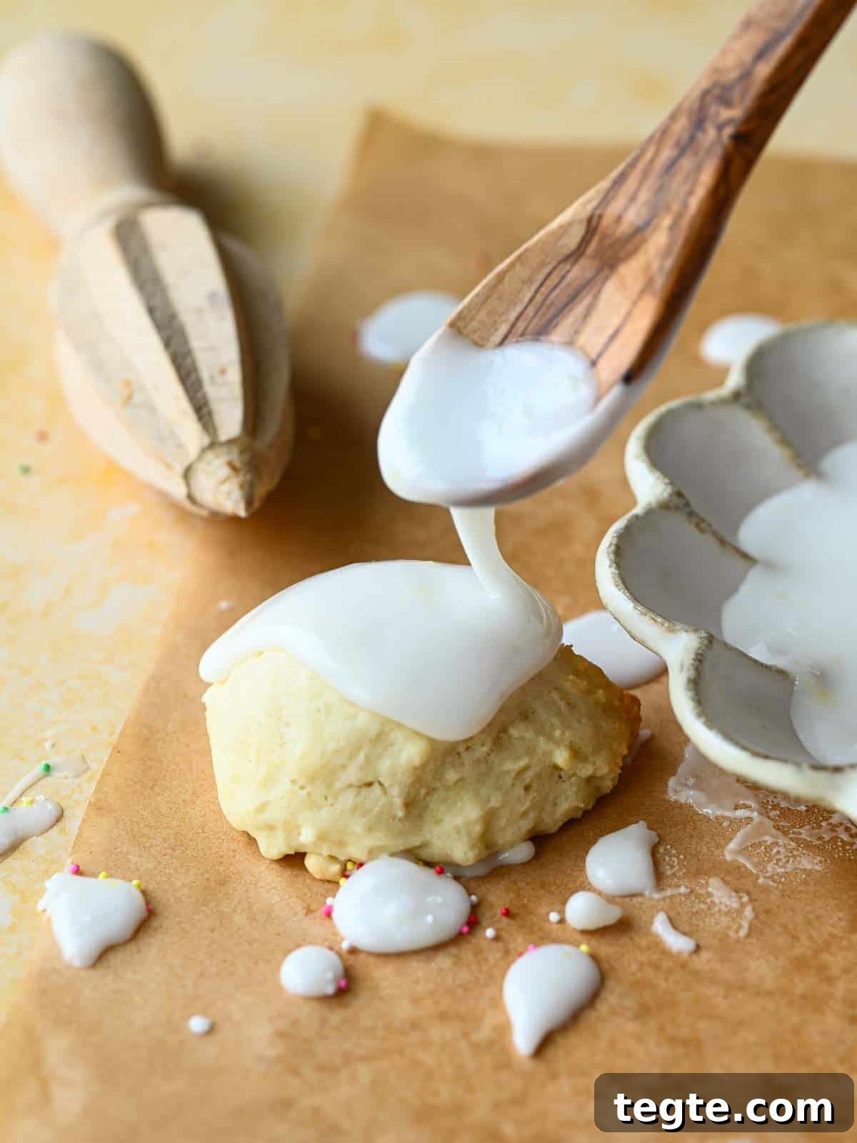 Italian Lemon Drop Cookies Recipe — Zesty Citrus Shortbread Tips 10 Lemon icing being dripped by a spoon over a cookie on top of brown parchment paper.