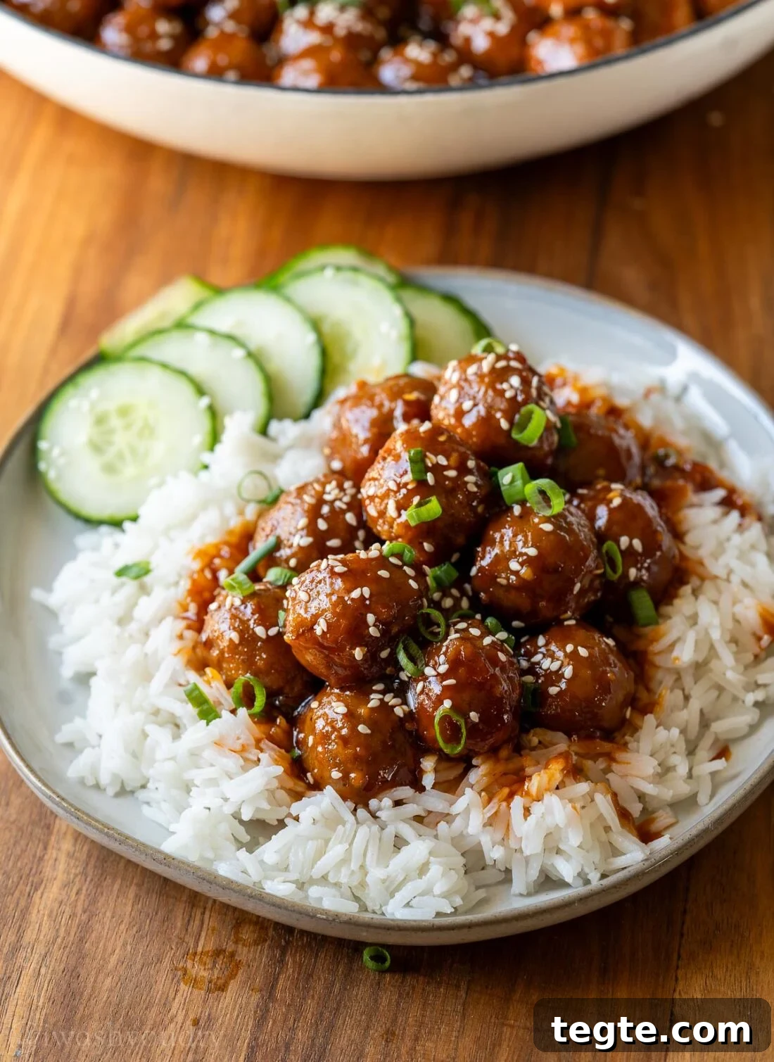 plate with korean bbq meatballs over rice with cucumbers on the side.