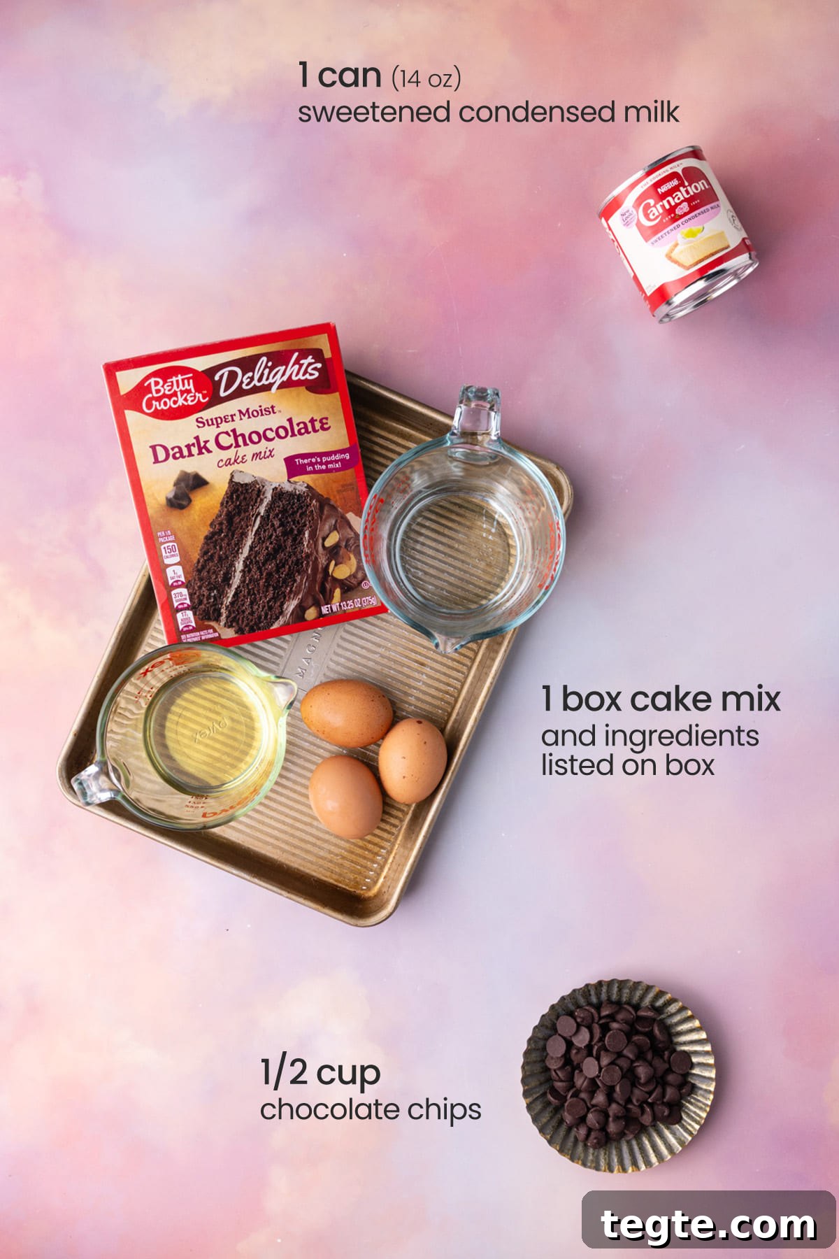Overhead view of the ingredients needed for chocolate poke cake - condensed milk, box cake mix on a tray with eggs, water and oil, and chocolate chips.