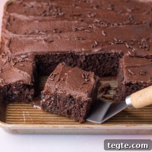 Taking a serving of chocolate poke cake off of the baking pan, showing the super-moist texture on the inside.