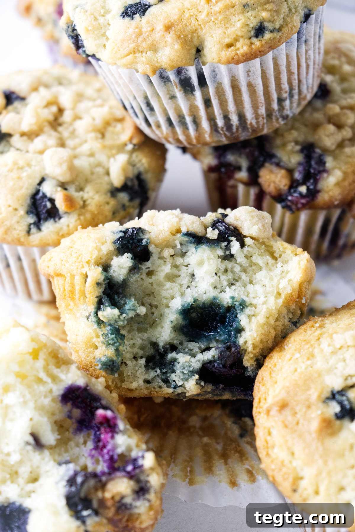 Sourdough Blueberry Muffins Recipe: Tangy, Moist, and Fluffy 3 A partially eaten blueberry muffin surrounded by more muffins.