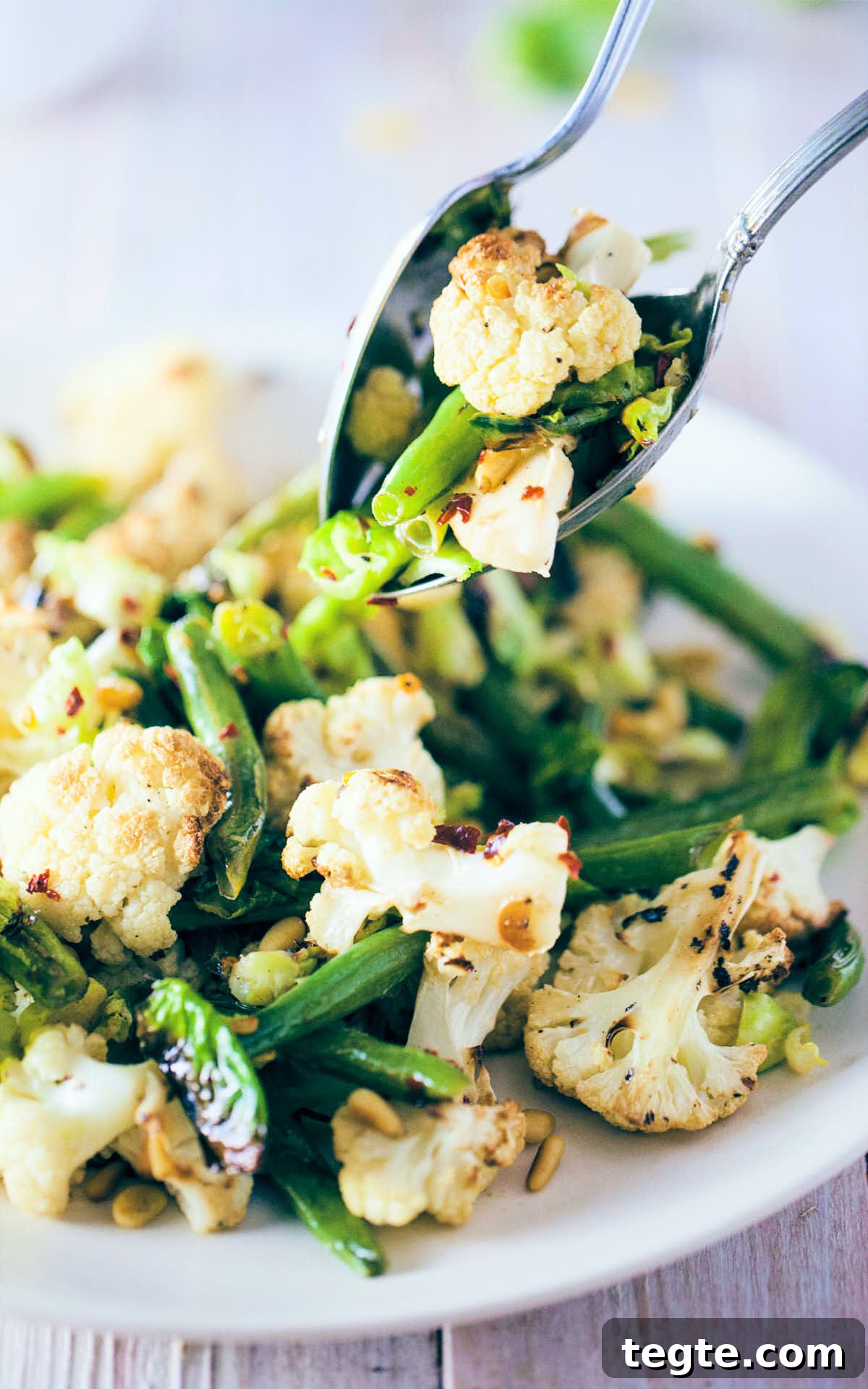 Scooping roasted cauliflower and brussels sprout salad with serving spoons