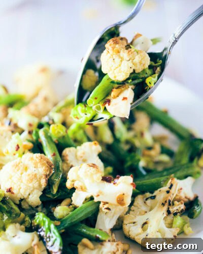 Scooping roasted cauliflower and brussels sprout salad with serving spoons