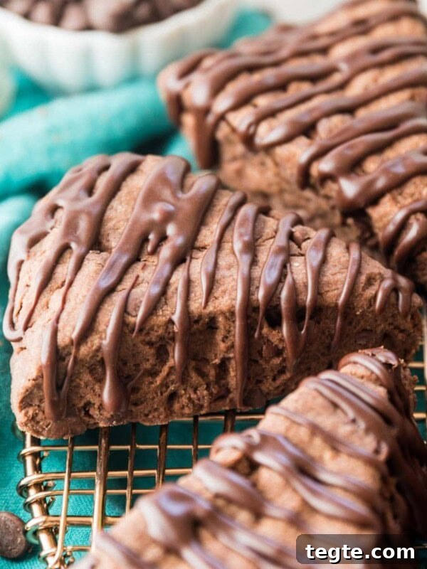 three wedge-shaped chocolate scones drizzled with a chocolate glaze on a metal cooling rack
