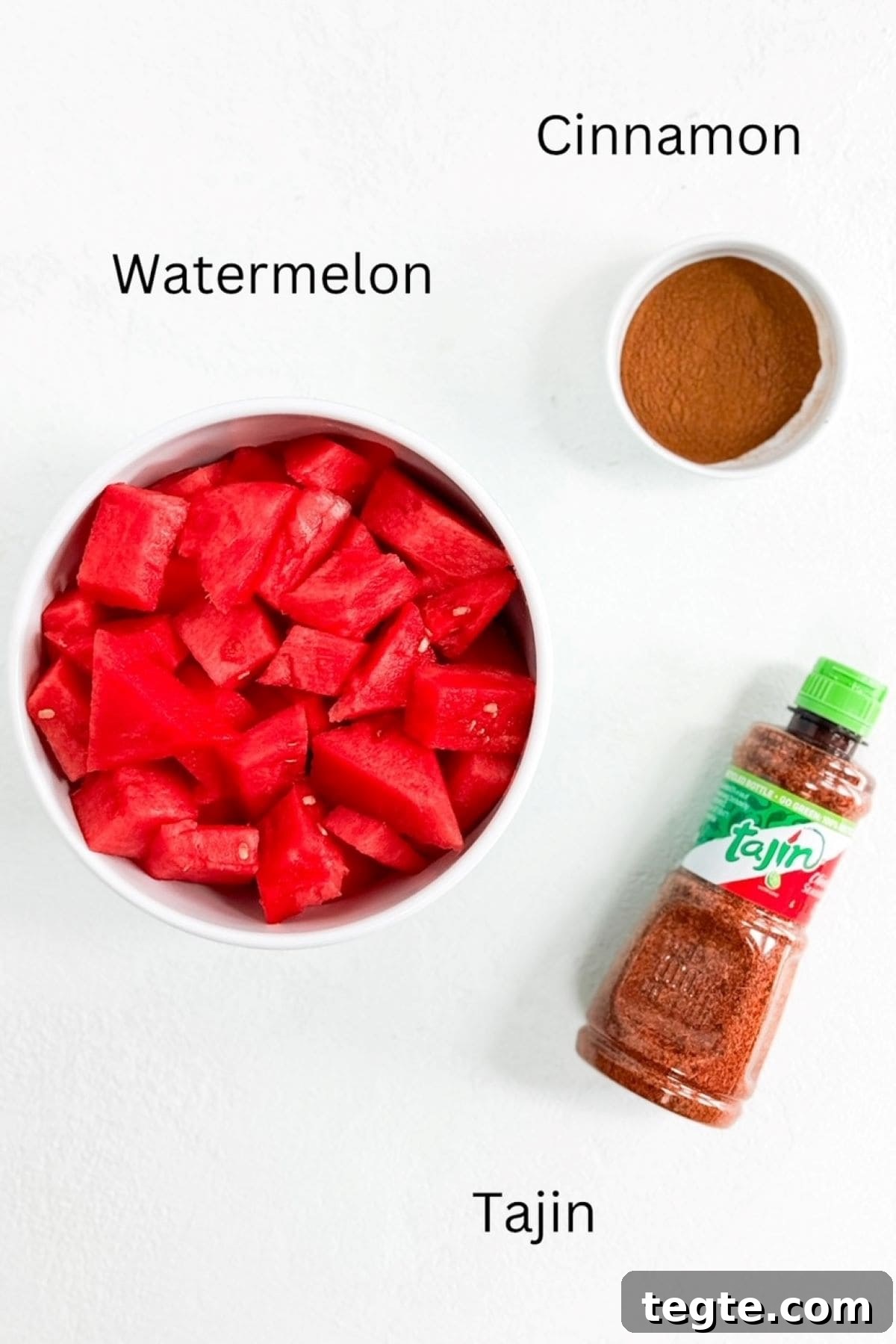 Watermelon in a bowl, cinnamon in a small bowl, and a bottle of Tajin.