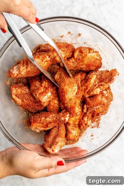221026_Dry Rub Chicken Wings-08 Hand holding a pair of tongs and tossing chicken wings in a dry rub spice mixture.
