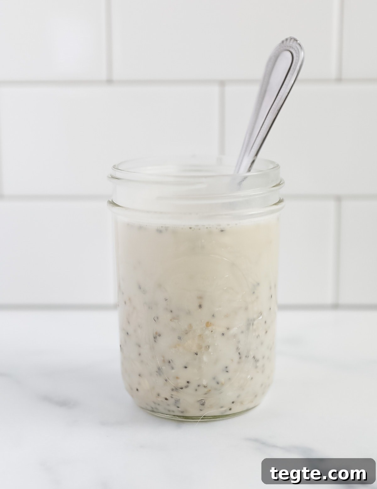 Creamy Chia Seed Overnight Oats Recipe for Quick Breakfast 4 A mason jar with unmixed oatmeal and plant based milk with a spoon in the jar