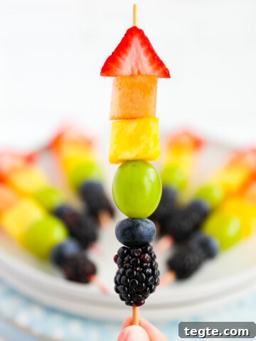 A fruit skewer with strawberry, melon, pineapple, grape, blueberry, and blackberry