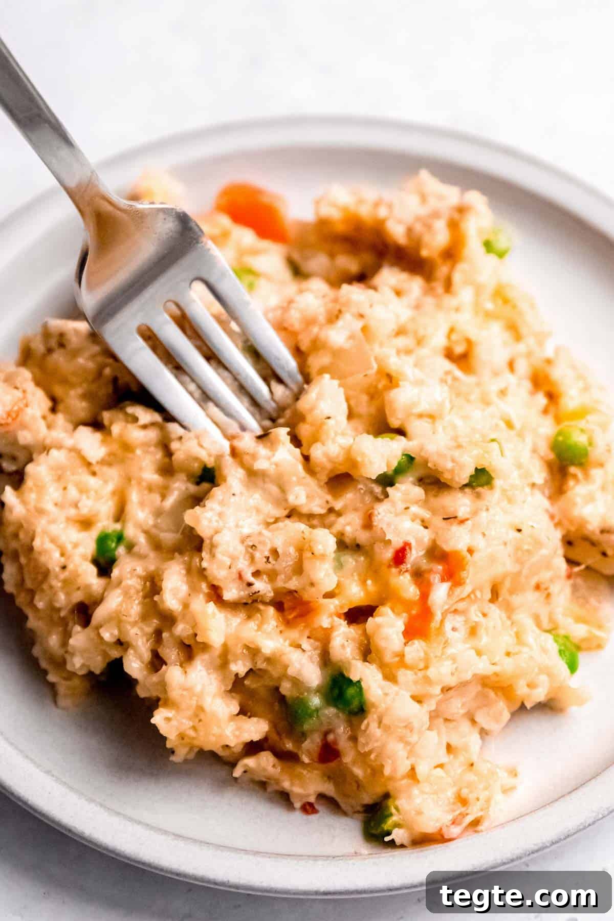 a fork in a big serving of chicken and rice with carrots and peas on a white plate
