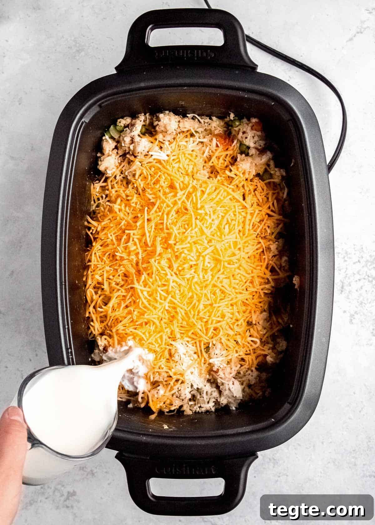 milk being poured into cheesy chicken and rice in a slow cooker