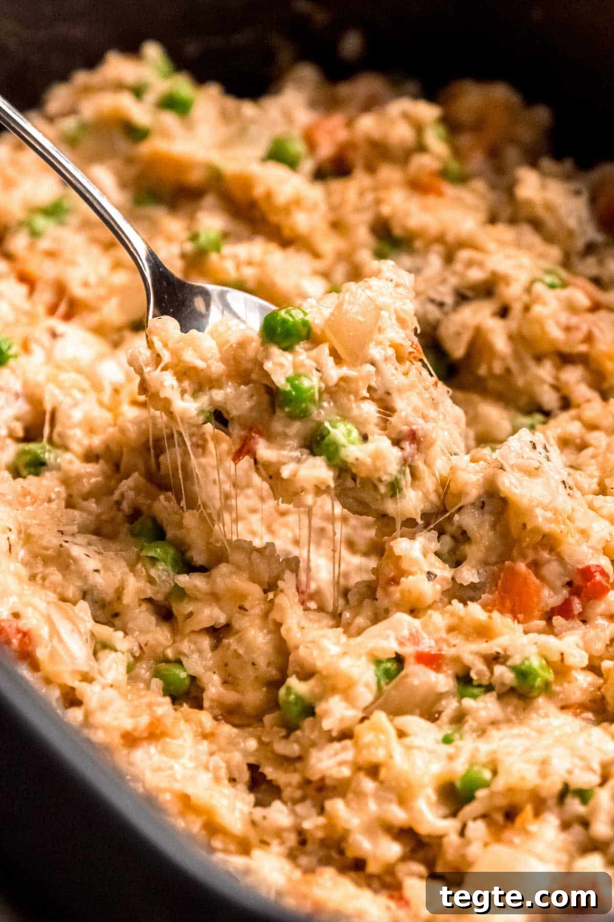 a big crockpot full of chicken, rice, peas, and carrots with gooey, melted cheese