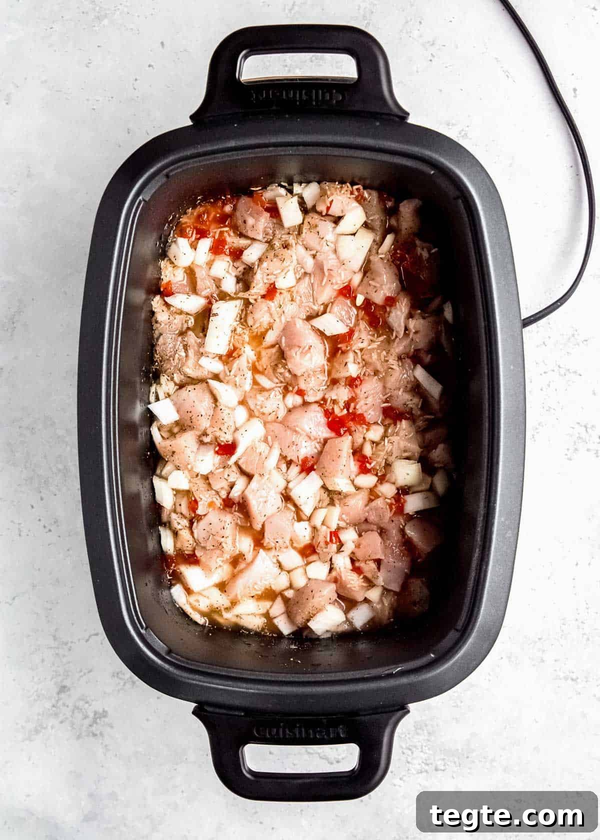 chicken and rice cooking in a crockpot with chopped onions, pimentos, and seasonings in chicken stock