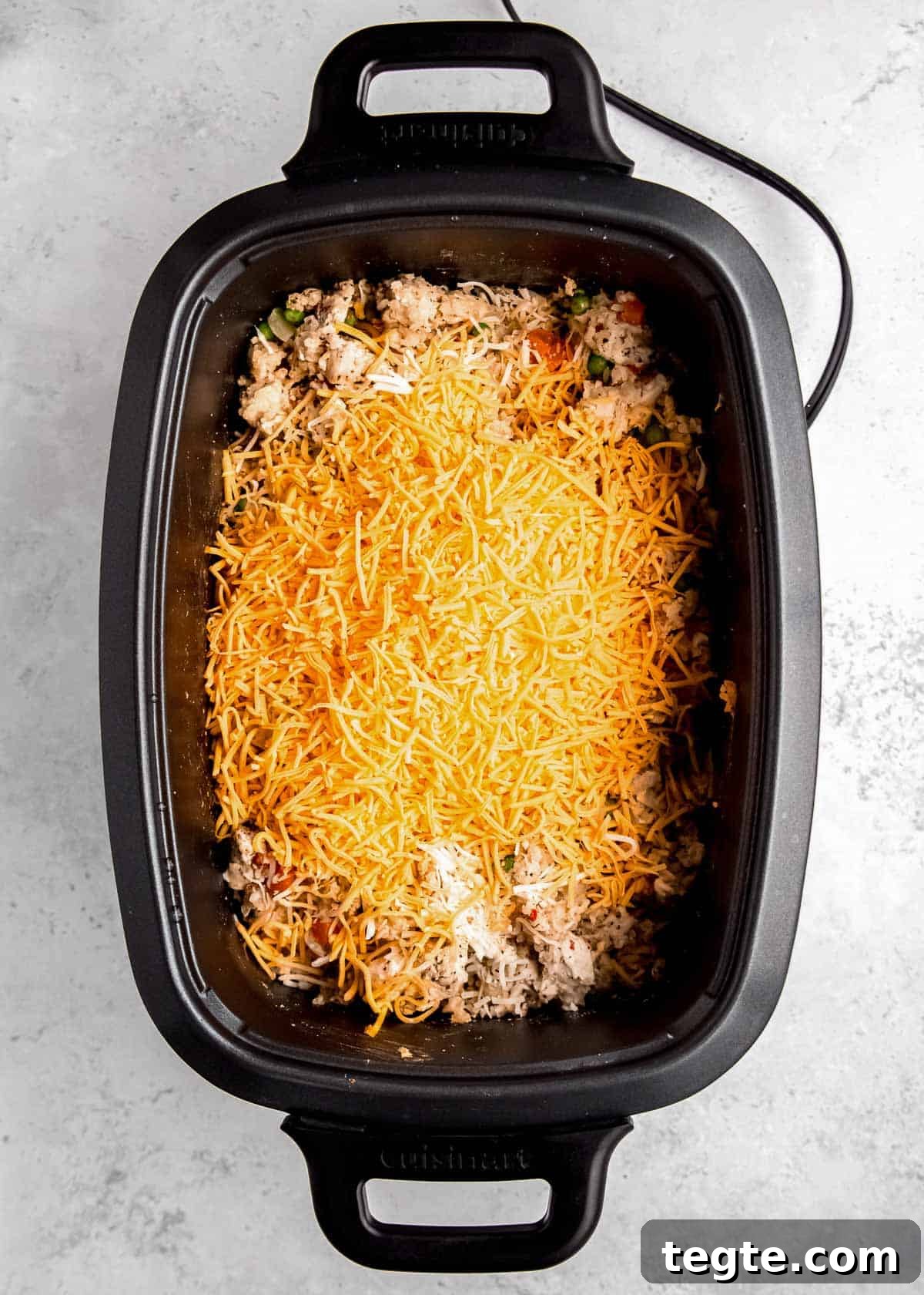 shredded cheese added to a crockpot full of chicken and rice