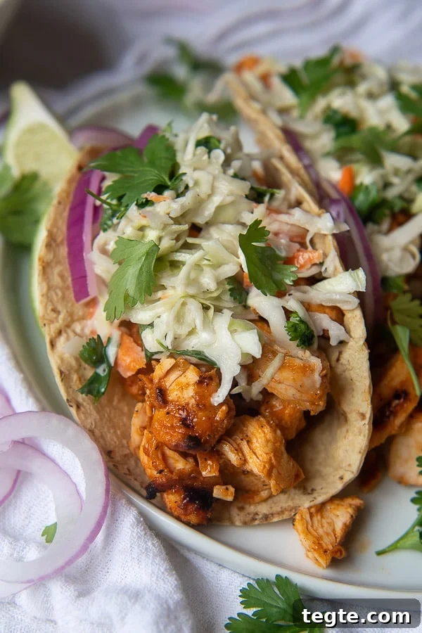Grilled Buffalo Chicken Tacos with Tangy Slaw and Marinade 2 a close up of buffalo chicken tacos with a blue cheese slaw on top with sliced red onions on plate