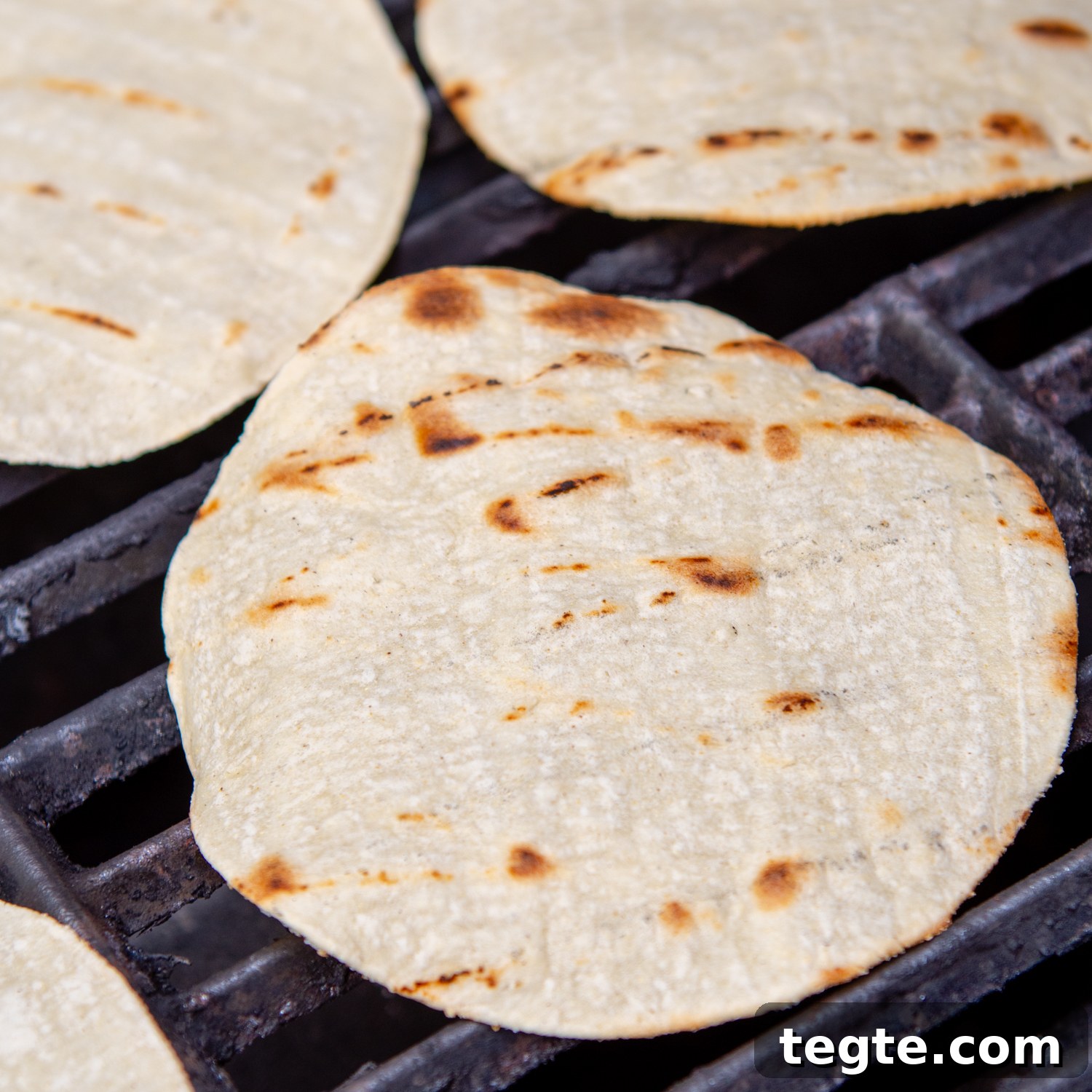 Grilled Buffalo Chicken Tacos with Tangy Slaw and Marinade 6 tortillas being charred slightly on a grill.