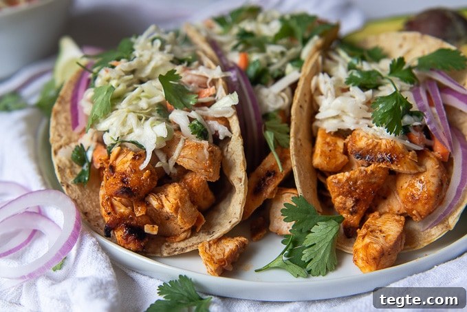 Grilled Buffalo Chicken Tacos with Tangy Slaw and Marinade 8 close up of two buffalo chicken tacos on a white plate with fresh cilantro scattered around
