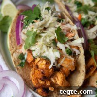 Grilled Buffalo Chicken Tacos with Tangy Slaw and Marinade 9 a close up of buffalo chicken tacos with a blue cheese slaw on top with sliced red onions on plate