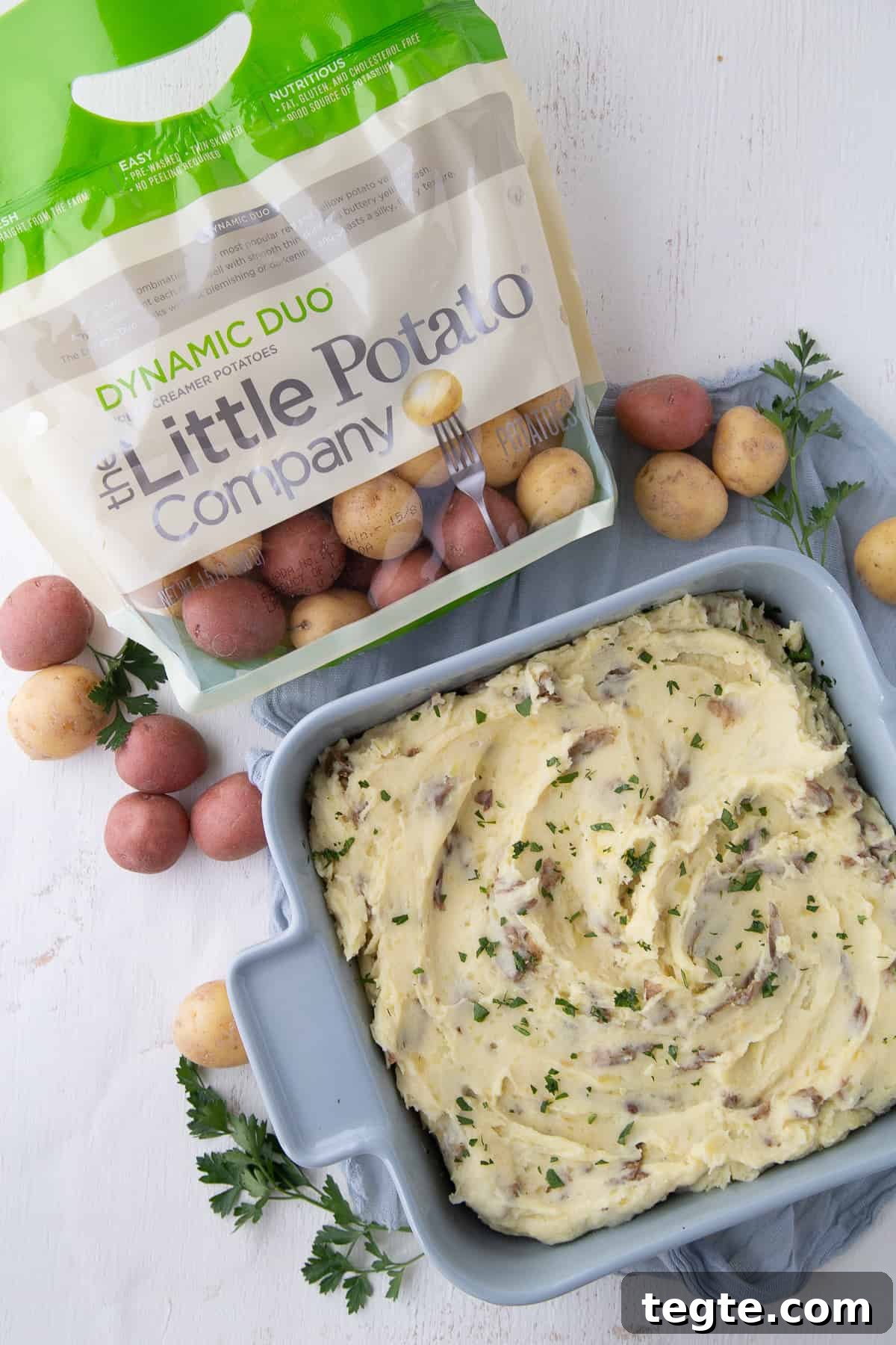 Creamy Mashed Potato Casserole Without Peeling Potatoes 2 blue square dish of mashed potatoes surrounded by small potatoes and a bag of The Little Potato Company potatoes.