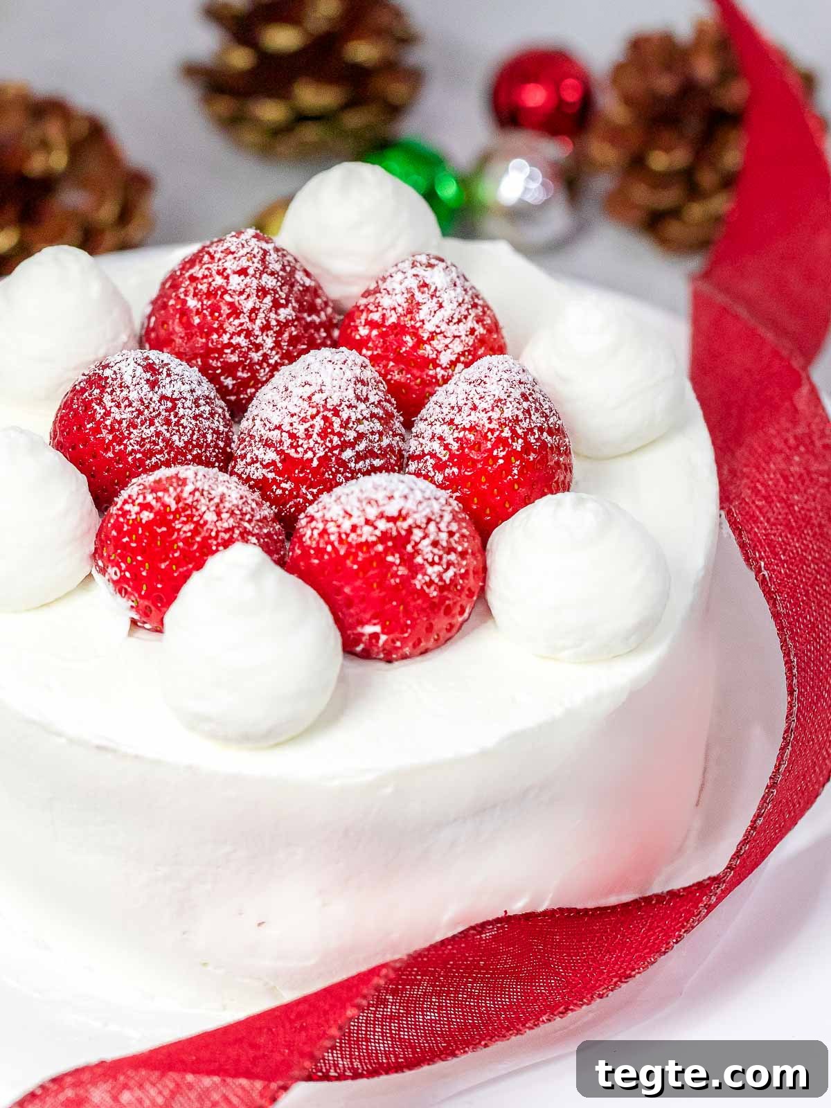Authentic Japanese Strawberry Shortcake Recipe — Fluffy, Light Slice 11 Japanese Christmas cake decorated with fresh strawberries and whipped cream next to red ribbon, Christmas ornaments, and pine cones in the background