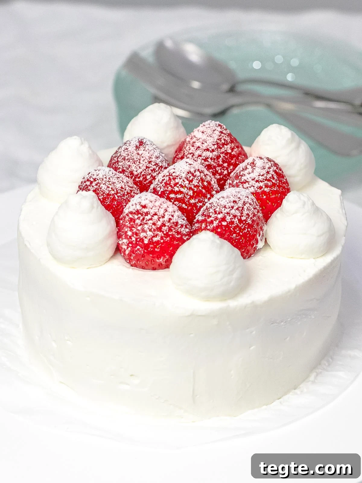 Authentic Japanese Strawberry Shortcake Recipe — Fluffy, Light Slice 5 Fresh strawberry cream cake decorated with whole strawberries, powdered sugar, and whipped cream next to plates and utensils