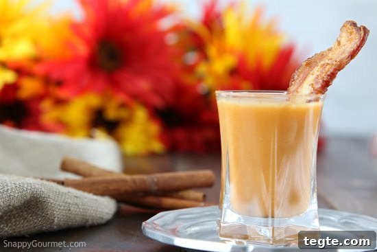 carrot soup shooter in shot glass with strip of bacon and cinnamon sticks in background with fall flowers