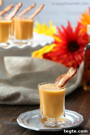 carrot soup shooter in shot glass with strip of bacon on plate with carrot soup shooters in background on cake stand