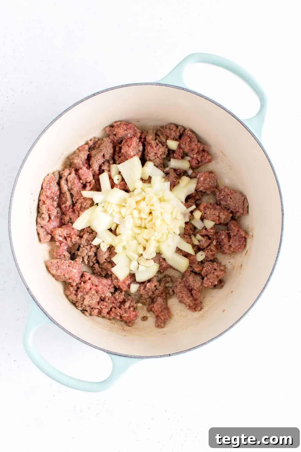 Diced onions and garlic added to ground beef in a pot.