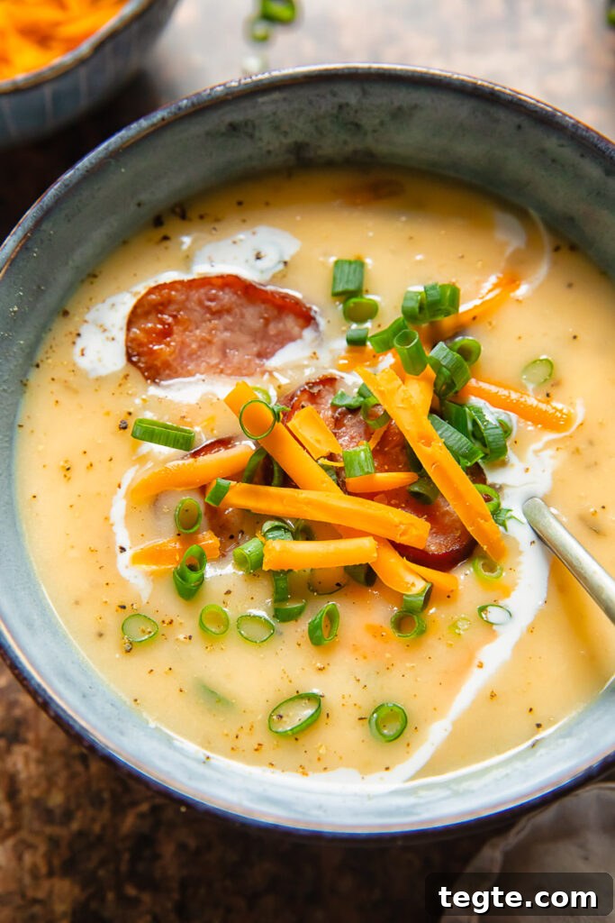 Hearty Kielbasa and Potato Soup Recipe 3 Close up shot of a spoon and bowl of kiebasa potato soup with single cream and herbs