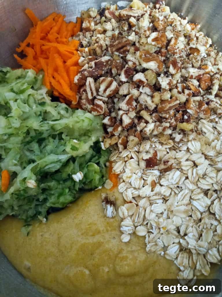 Zucchini Bars with Cream Cheese Frosting Recipe for Moist Dessert 3 ingredients piled into a mixing bowl with some of the batter: shredded zucchini, oats, pecans, and shredded carrots.